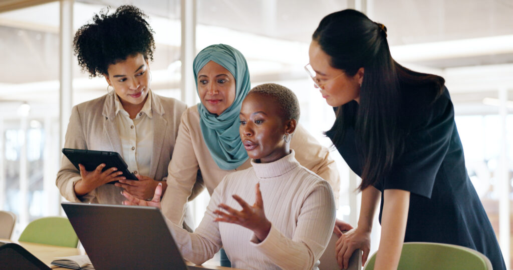 A group of women are collaborating on a project while using laptops in an office setup.